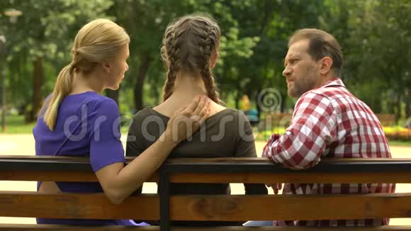 爱的父母支持沮丧的女儿坐在公园的长凳上悲伤视频的预览图