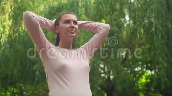 公园里的一个怀孕的女孩在绿柳的背景下一个平静的女孩站着双手抱在脑后视频的预览图