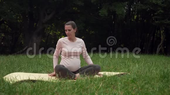 孕妇在公园里做瑜伽的地毯上摆姿势莲花坐在一个姿势腿伸展视频的预览图
