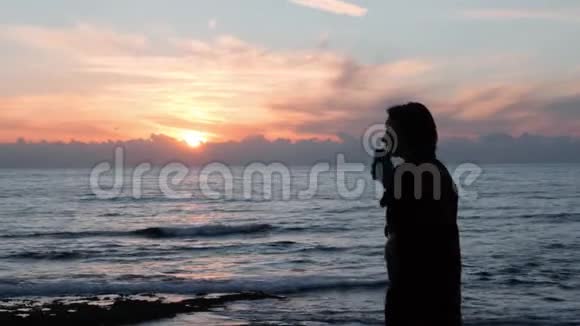 在洛奇海岸打电话的小女孩在海上夕阳下打电话的女孩剪影迷人的女人微笑着视频的预览图