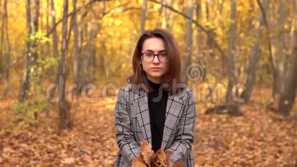 一个戴眼镜的年轻女子在秋天的森林里把黄叶扔了上来慢动作视频的预览图