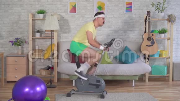 有趣的男子运动员从80带着胡子从运动自行车上摔下来在沙发上慢悠悠视频的预览图