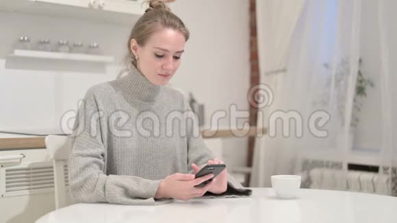 有魅力的年轻女性在家里使用智能手机视频的预览图