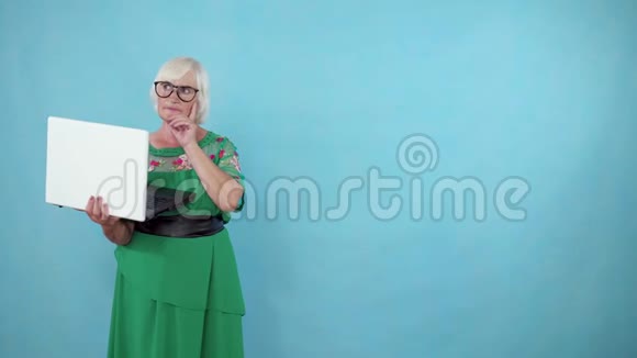 一位体贴的老妇人手里拿着笔记本电脑找到了解决办法站在蓝色背景的复印空间上视频的预览图
