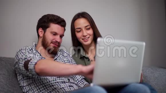 已婚夫妇坐在柔软的沙发上在客厅里看着笔记本电脑视频的预览图