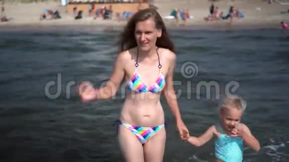 苗条的母亲和可爱的小女儿在海滩上的海浪中行走视频的预览图