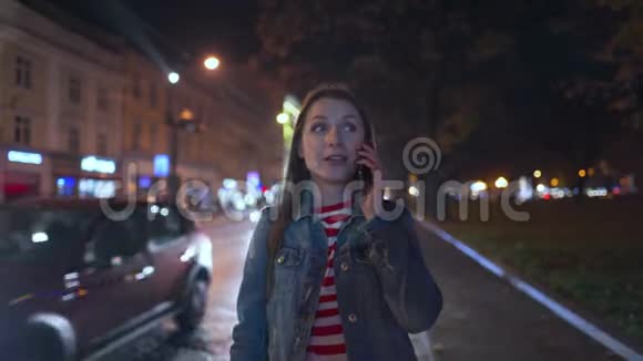 女人和她的朋友在智能手机上交谈看到他在街上打电话来接近她城市灯火模糊视频的预览图