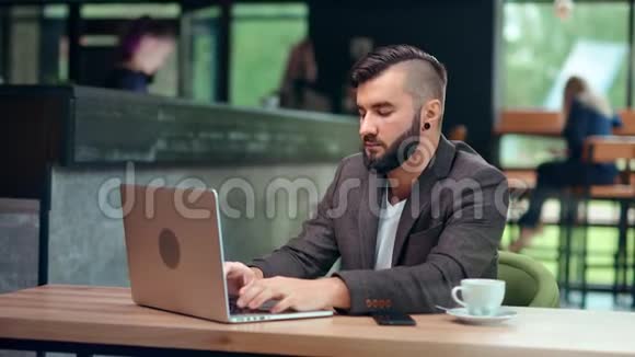 年轻的自由职业者有着时髦发型坐在公共咖啡馆的笔记本电脑上工作视频的预览图