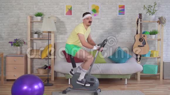 有趣的是80多岁的留着胡子的疲惫的运动员正在家里骑着一辆运动自行车慢悠悠地视频的预览图