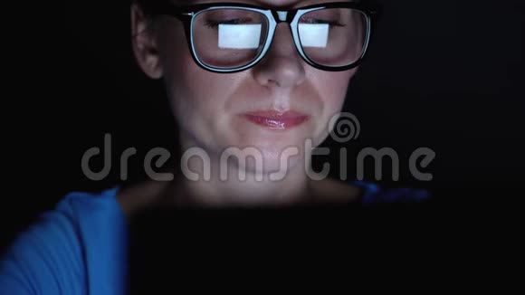 戴眼镜的女人晚上在笔记本电脑后面工作监视器屏幕反映在眼镜上视频的预览图