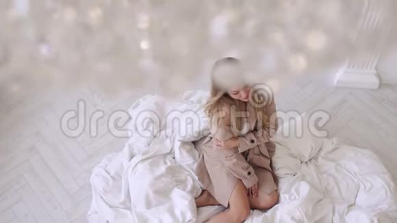 穿着米色外套的性感女孩坐在明亮的房间里地板上的白色毯子上视频的预览图