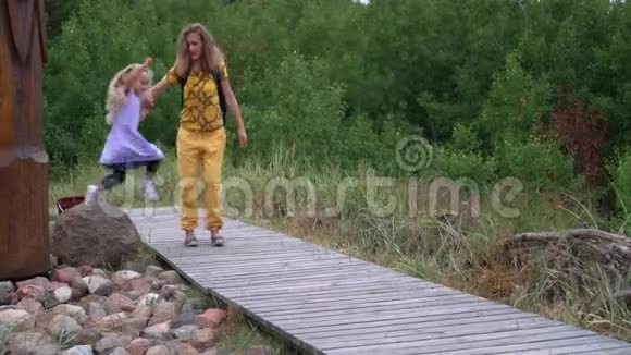 小女孩从大石头上跳下来和妈妈一起走过木路视频的预览图
