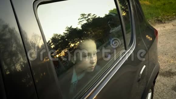 一个脸上长着雀斑的迷人小女孩透过车窗看着天空和日落视频的预览图