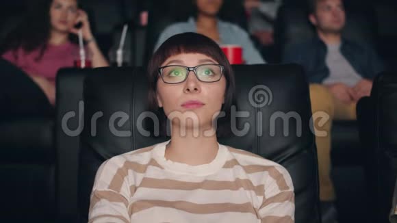 戴眼镜的漂亮女孩在电影院看悲伤电影摸着敏感的脸视频的预览图