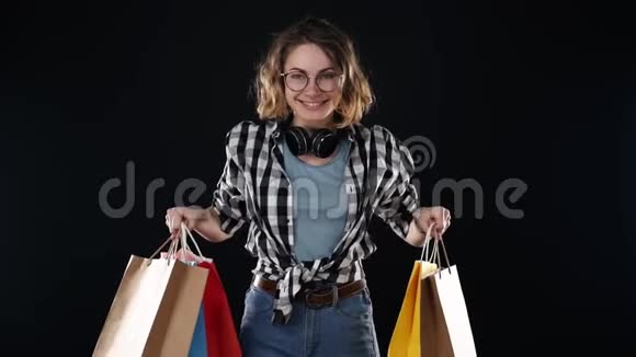 戴着眼镜戴着耳机脖子上戴着五颜六色的购物袋的欧洲年轻女性视频的预览图