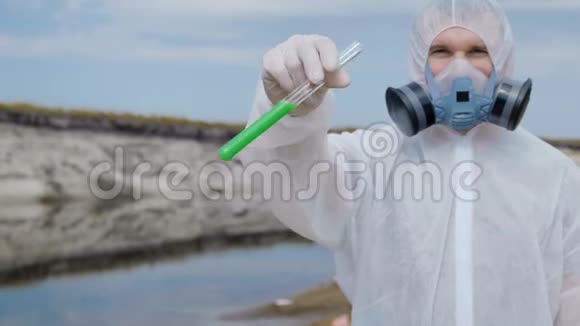 一个穿着防护服和呼吸器的人从靠近河边的试管中倒入一种化学物质视频的预览图