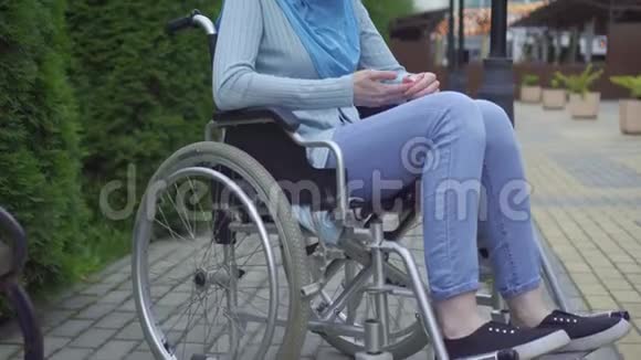 肖像孤独悲伤的年轻穆斯林妇女残疾的传统围巾坐在公园的轮椅上视频的预览图