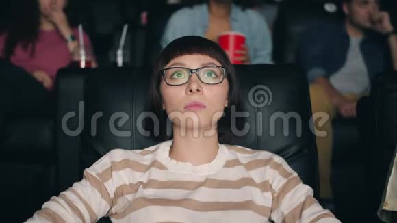 在电影院看恐怖惊悚片的被吓坏的年轻女士盯着屏幕视频的预览图