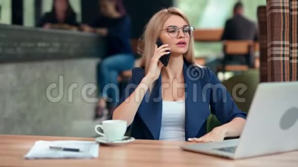 自信时尚的商务女性在咖啡馆里坐在桌子上用智能手机说话视频的预览图