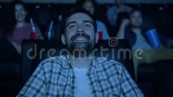 快乐的黑发人在电影院看滑稽电影在黑暗的房间里笑着玩视频的预览图