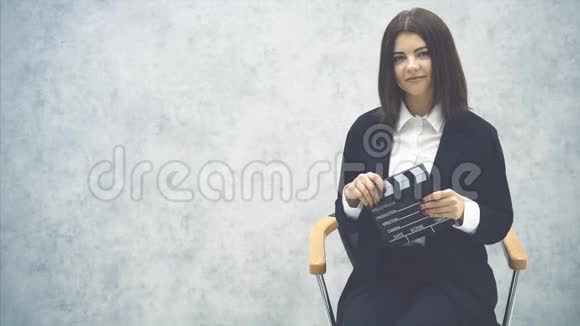 可爱的年轻女孩坐在椅子上在她的面前拍手板摆姿势微笑视频的预览图