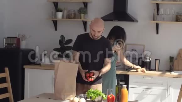 一个女人做饭男人带着纸袋的食物把蔬菜和水果从纸袋放在桌子上视频的预览图