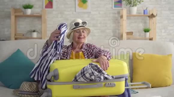 一位体贴微笑的退休妇女手里拿着一个手提箱坐在沙发上视频的预览图