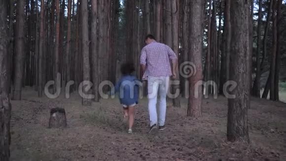 快乐的爸爸和女儿牵着手在森林里的一排排松树之间奔跑在周末的晚上慢动作视频的预览图