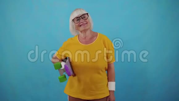 戴眼镜手拿滑板蓝底的积极运动的老妇人视频的预览图