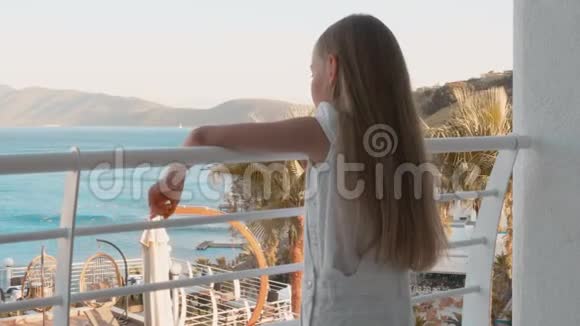 站在阳台度假酒店的年轻女孩年轻女孩在酒店里看海景和游泳池游客视频的预览图