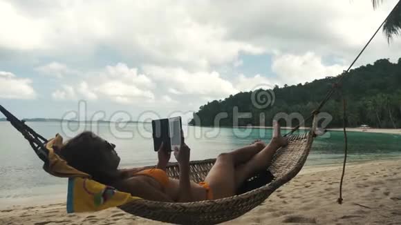 女孩在热带海滩的吊床上放松和阅读视频的预览图