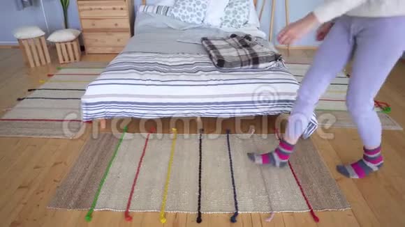 一个穿着家居服的女人走在针织的床头地毯上纠正她的棕色粉红色袜子视频的预览图