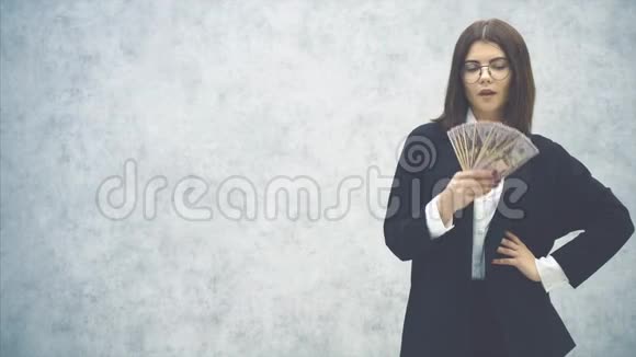 可爱的年轻女商人穿着正式的西装她的手akimbo挥舞着一把钞票的扇子靠近她的脸使风它视频的预览图