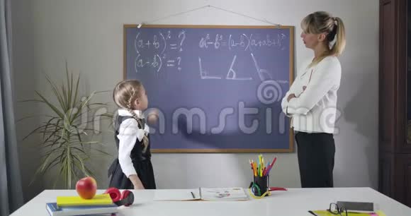 漂亮的白人女孩穿着优雅的校服中年家庭教师站在黑板前学习数学视频的预览图