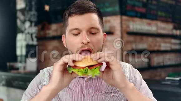 饥肠辘辘的大胡子年轻苗条的男人喜欢吃美味的汉堡看着相机感到快乐视频的预览图