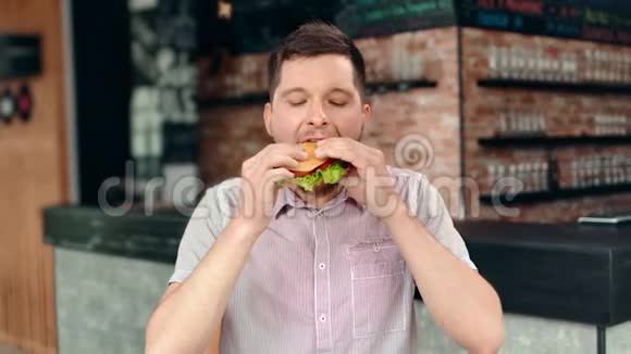快乐的年轻男性咬多汁汉堡享受令人惊叹的美味积极的情绪视频的预览图