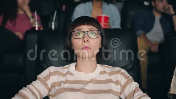 戴眼镜的吓坏了的女孩在电影院看恐怖电影用手闭上眼睛视频的预览图