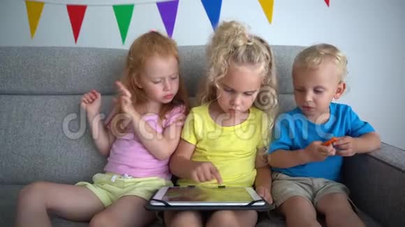 孩子们坐在沙发上分享一台平板电脑沮丧的红发女孩视频的预览图