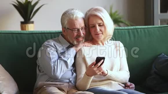 老太太和丈夫坐在沙发上使用智能手机应用程序视频的预览图