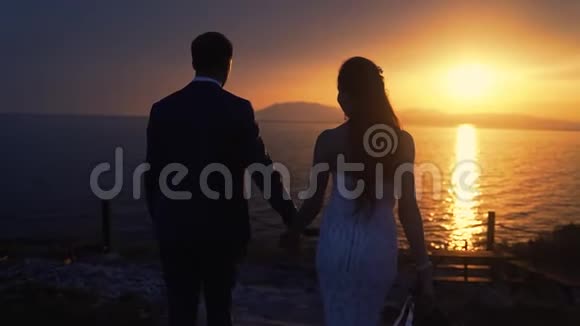新婚夫妇在夕阳的背景下漫步在海洋中慢动作视频的预览图