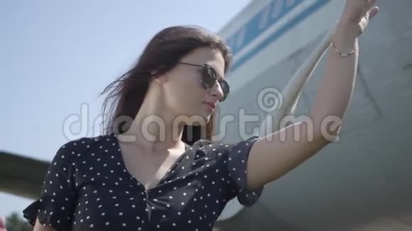 年轻的黑发女孩戴着太阳镜手里拿着白色披肩站在大飞机前望着远处视频的预览图