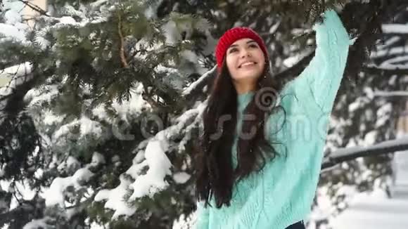 一位年轻貌美的女士穿着一件温暖的针织蓝色毛衣和一顶红色帽子正玩得很开心微笑着小跑着一辆覆盖着雪的车视频的预览图