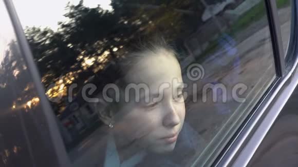 特写一个可爱的小女孩的脸她在天空和日落时仔细地透过汽车的玻璃看着视频的预览图