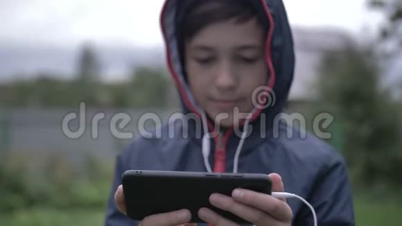 头罩里的男孩用手机在户外靠近玩游戏视频的预览图