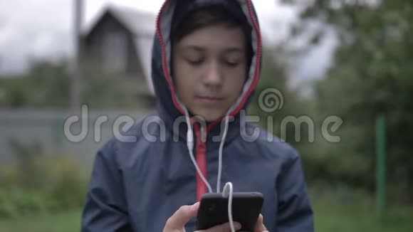 有耳机的男孩音乐爱好者在户外通过电话听音乐视频的预览图
