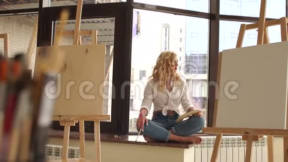 性感的女孩坐在窗台上画室里有画笔和画架视频的预览图