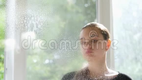 女性清洁窗户在玻璃上喷洒清洁剂水滴滴下视频的预览图