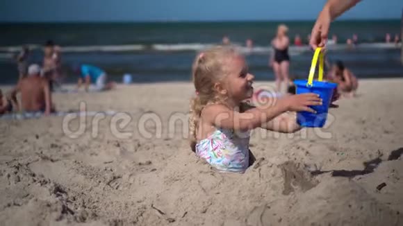 埋葬的小女孩拿着玩具桶和妈妈的水倒在沙子上视频的预览图