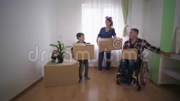 幸福的家庭与残疾父亲在婴儿车与盒子在手站在新的公寓并讨论安排视频的预览图