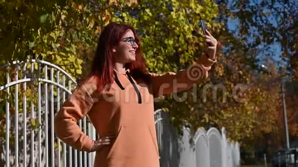 戴眼镜的漂亮红发女人在手机上自拍一个穿着赭色连帽衫的快乐女孩被拍到视频的预览图
